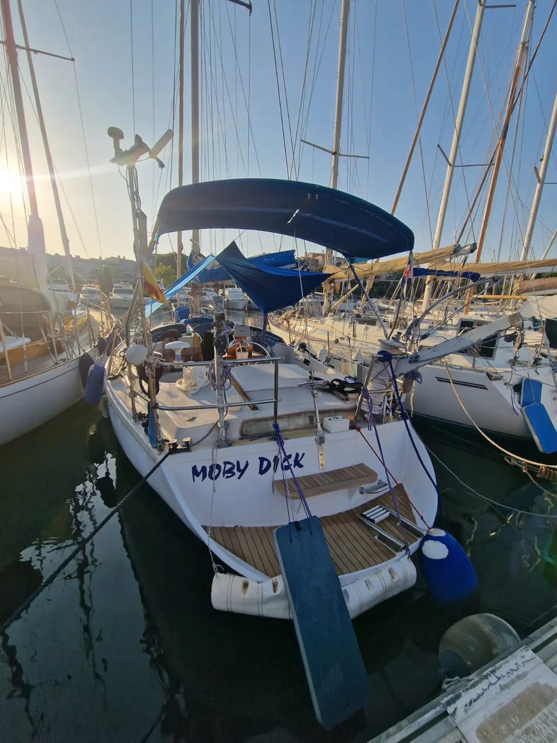 Gibert Marine gin fizz — Voilier blanc vu de poupe, amarré dans un port parmi d'autres bateaux.