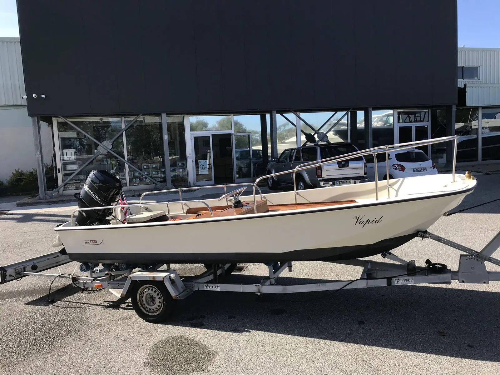 Boston Whaler 17 — Bateau à moteur blanc sur remorque, photographié de profil devant un bâtiment.