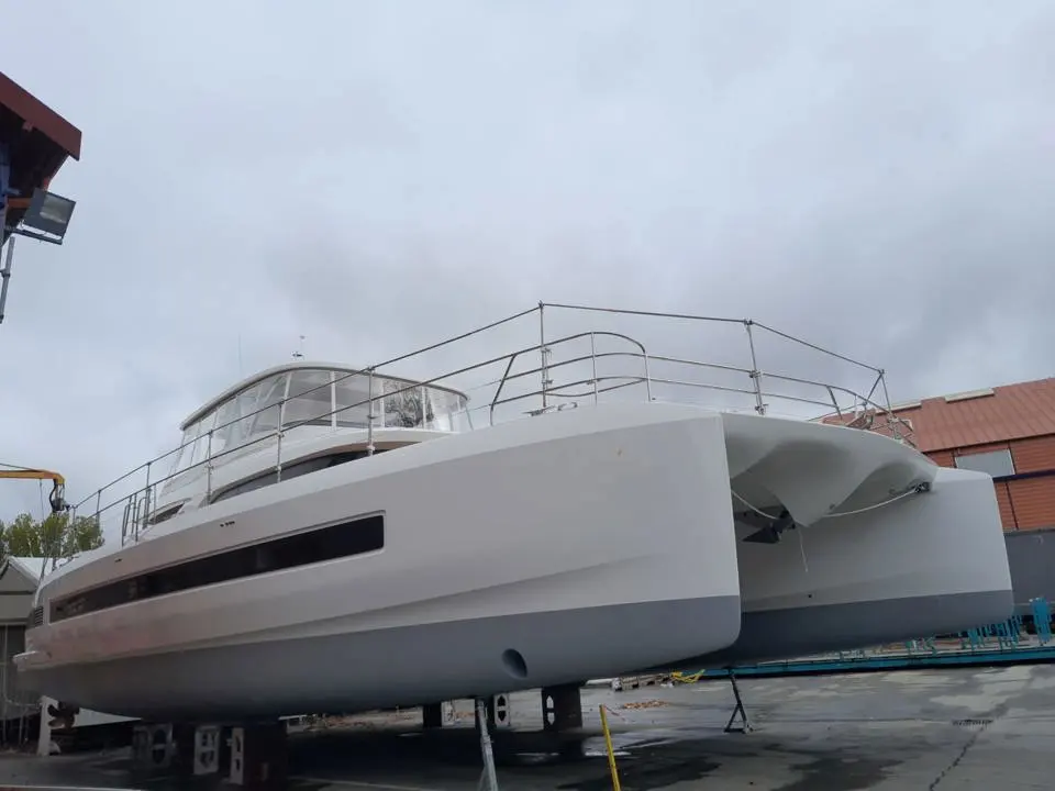 Lagoon Sixty 7 — Catamaran blanc vu de l’avant, posé à terre dans un chantier naval.