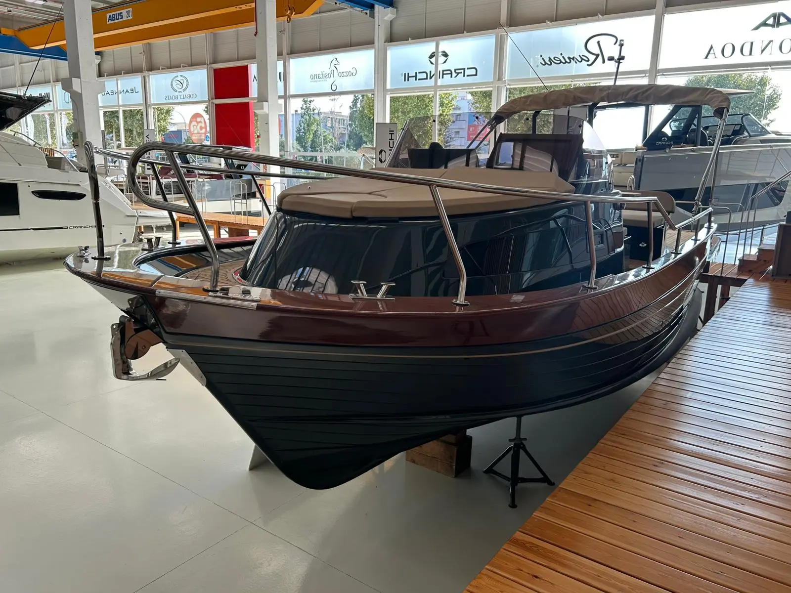 Gozzo Positano 28 Sole — Bateau à cabine présenté sur un support dans un showroom nautique.