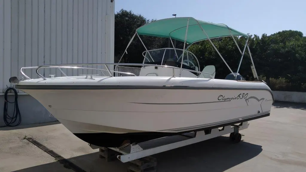 Ocqueteau Olympio 630 — Bateau à moteur blanc avec console centrale et taud vert, présenté sur remorque.
