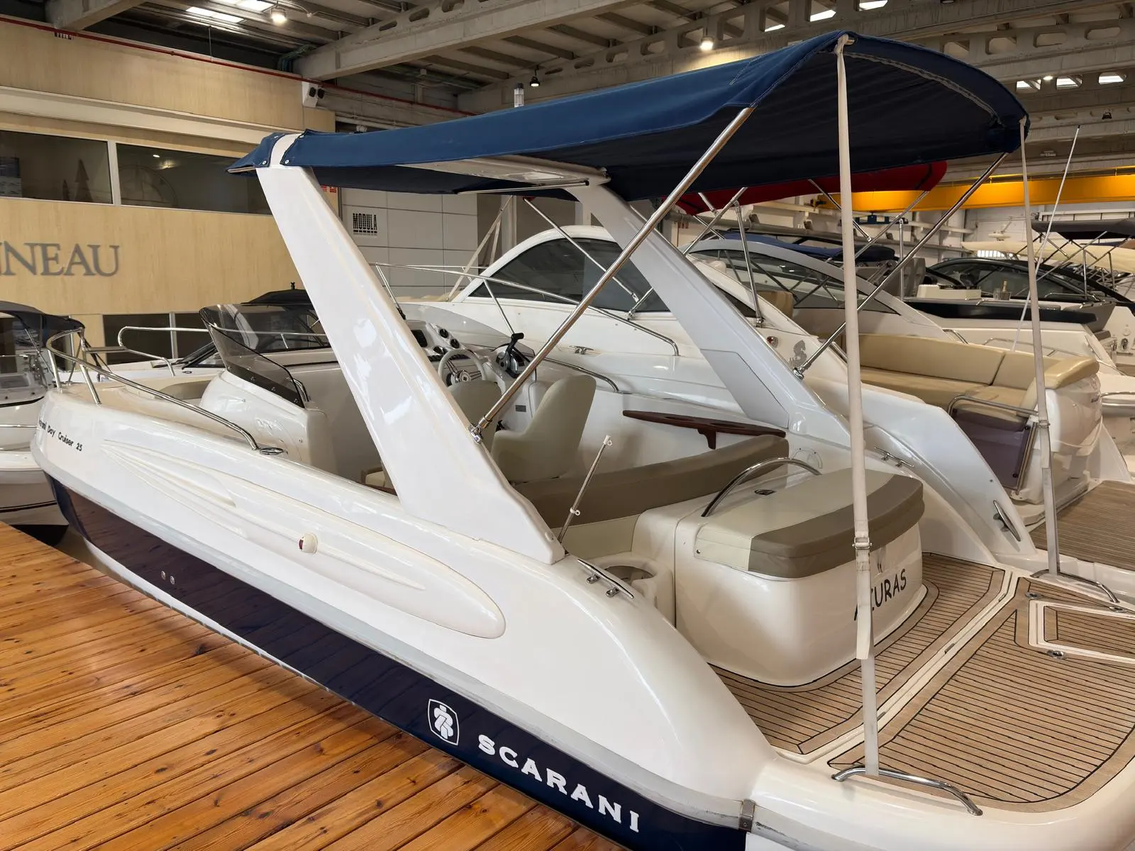 Scarani 25 Day Cruiser — Bateau blanc exposé en intérieur, vu de trois quarts arrière sous une toile bleue.