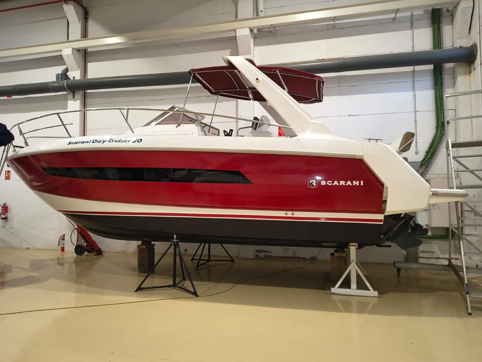 Scarani 30 Day Cruiser — Bateau à coque rouge présenté de profil dans un hangar, posé sur berceau.