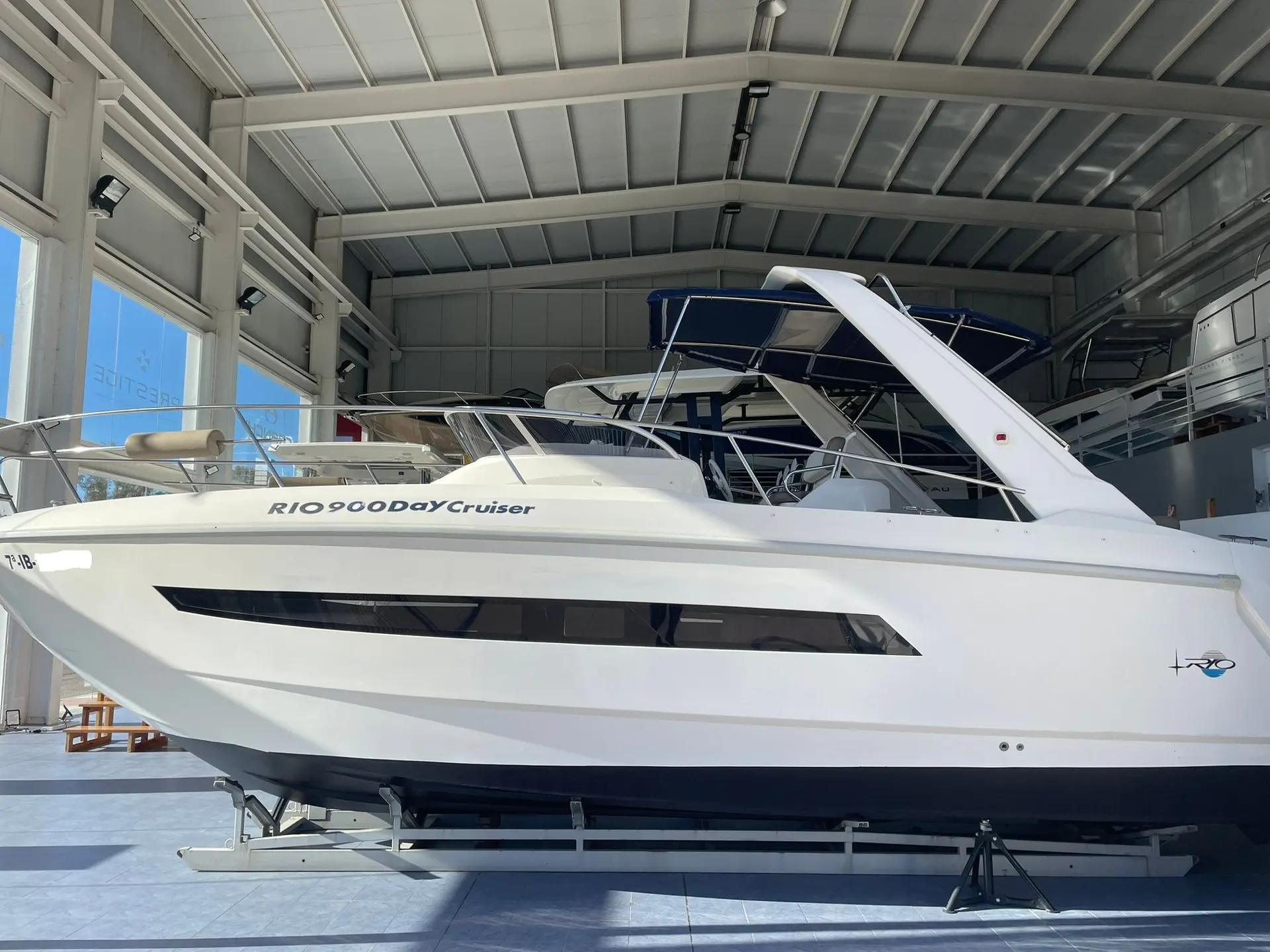 Rio 900 Day Cruiser — Vue latérale d’un bateau blanc exposé sur ber dans un hangar couvert.