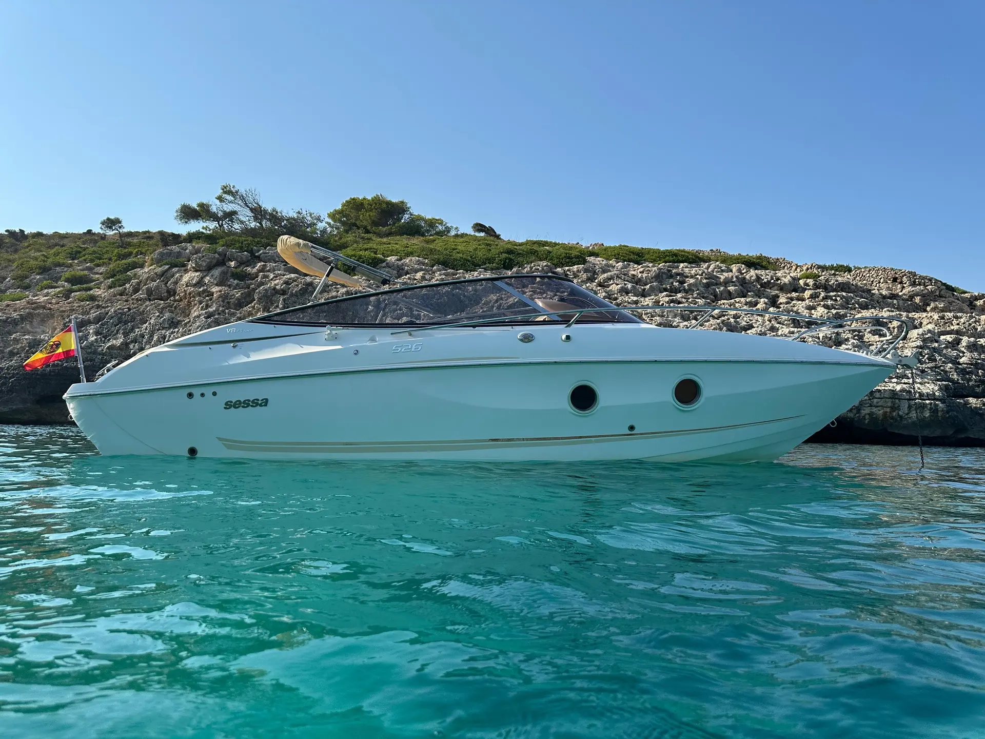 Sessa Marine S26 — Bateau à moteur vu de profil sur une eau turquoise, devant une côte rocheuse.