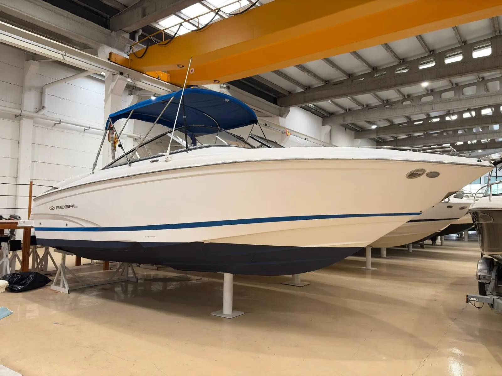 Regal 2700 — Bateau à moteur blanc et bleu présenté sur bers dans un hangar.