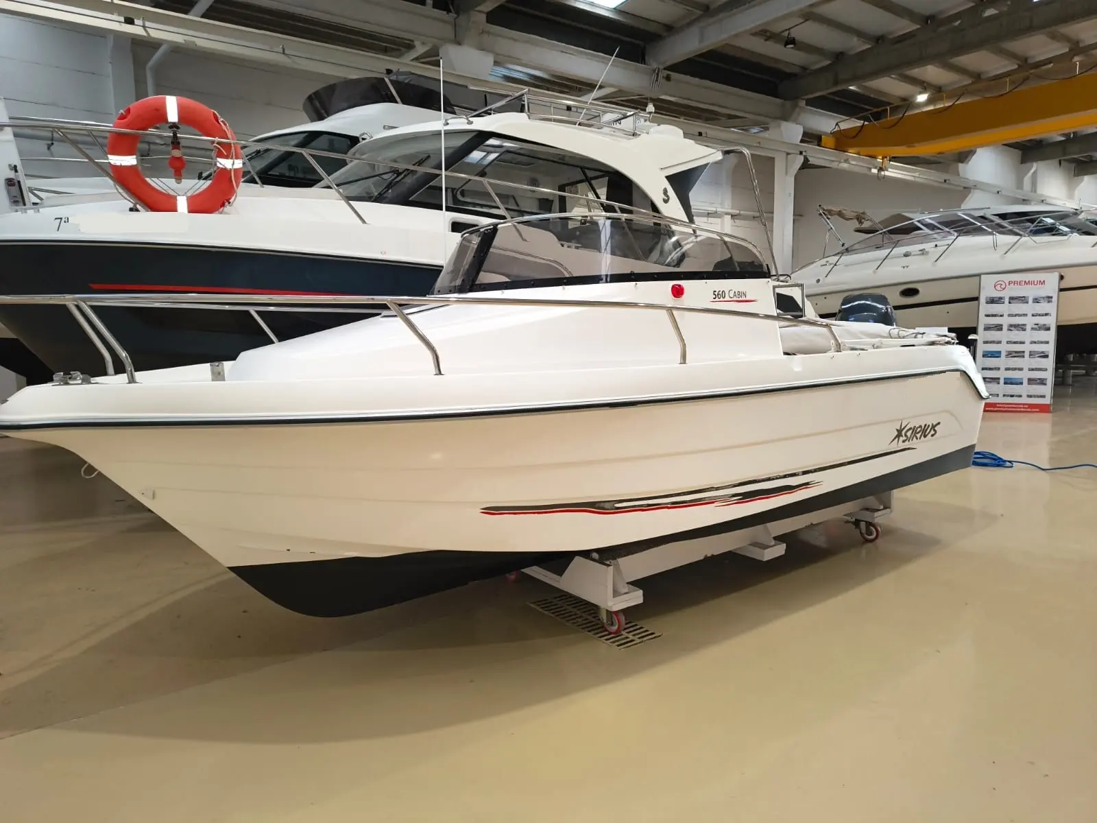 Sirius 560 Cabin — Bateau à moteur blanc exposé en intérieur, vu de trois quarts avant.