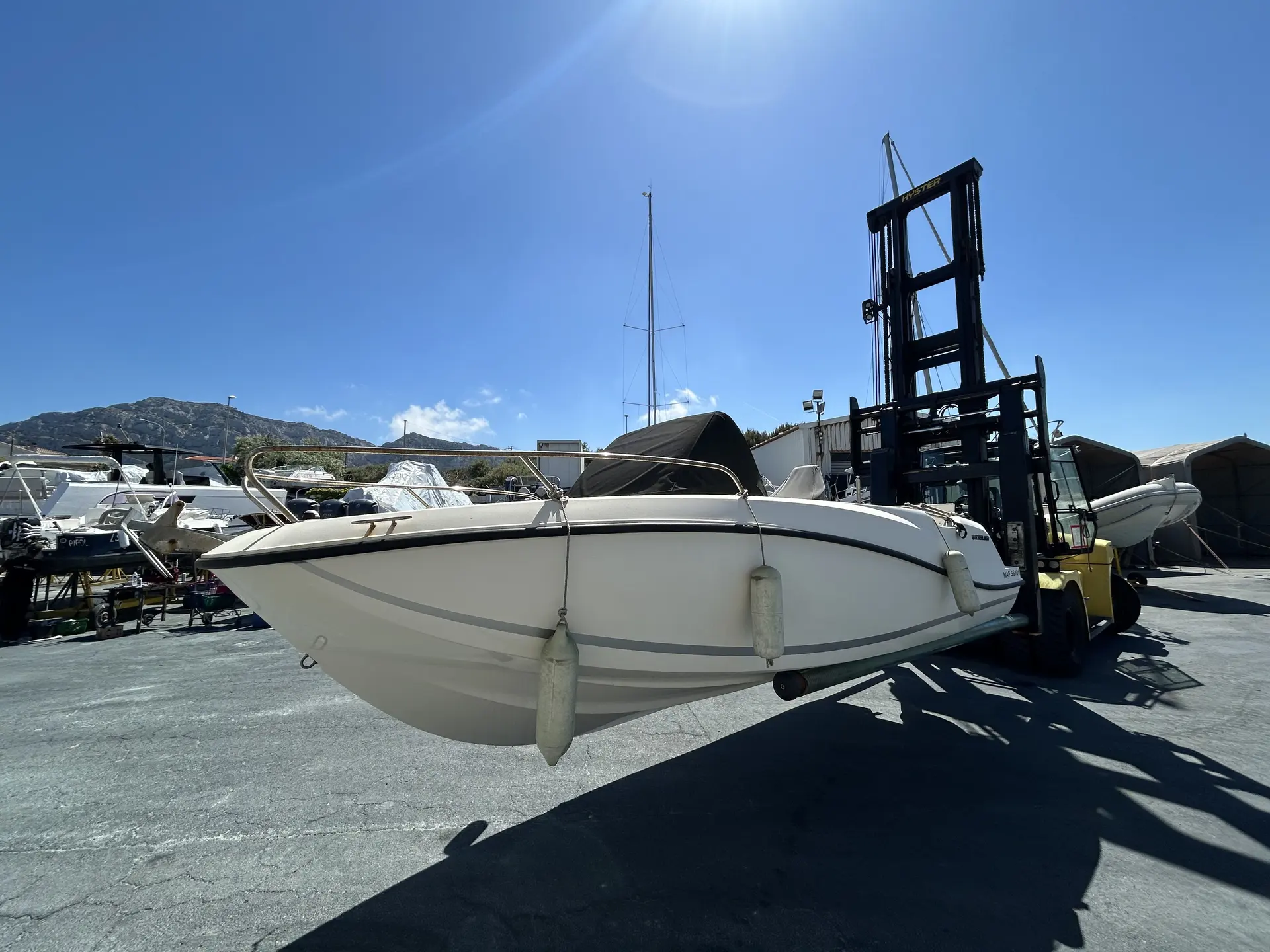 Quicksilver 605 Sundeck — Bateau blanc vu de trois quarts sur une aire de stockage nautique.
