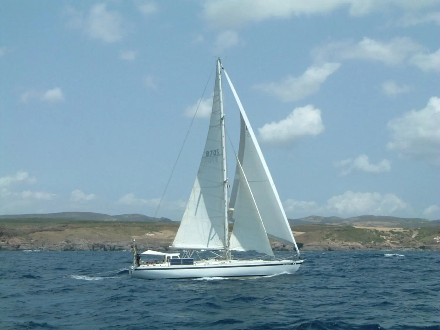 Pouvreau Meridien — Voilier blanc sous voiles naviguant au large d’une côte rocheuse