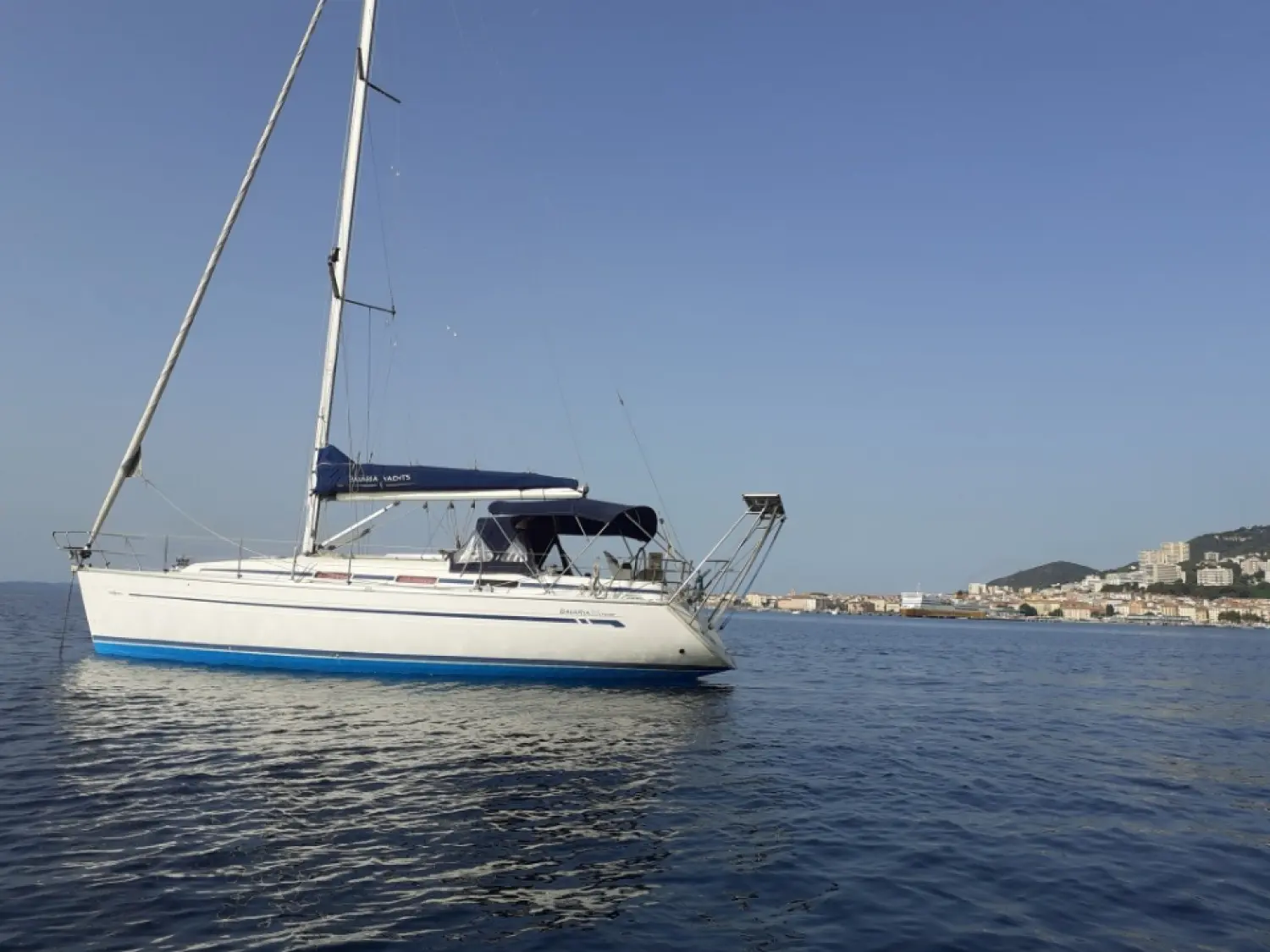 Bavaria 36 — Voilier blanc photographié au mouillage, avec une ville côtière en arrière-plan.