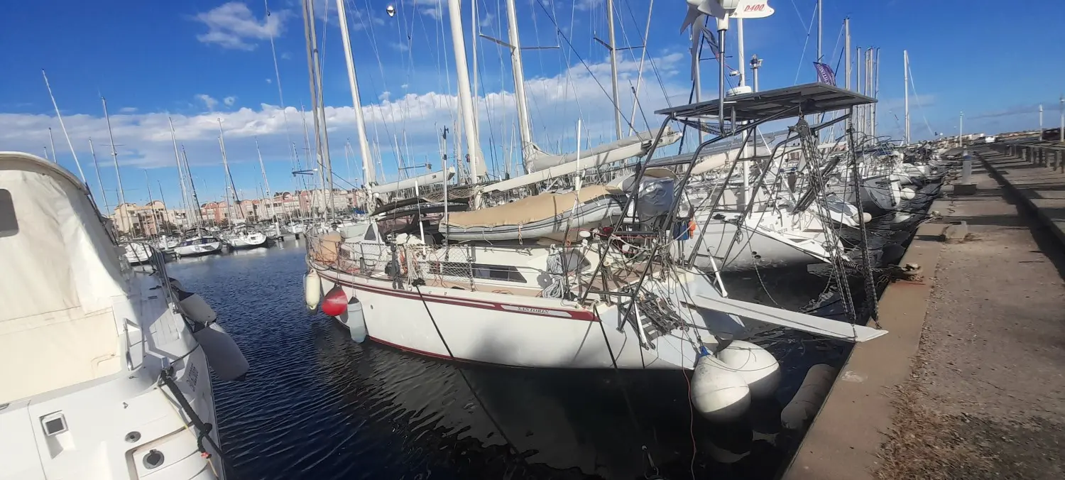 Amel Santorin Ketch — Voilier amarré dans un port, entouré d'autres bateaux et de mâts.