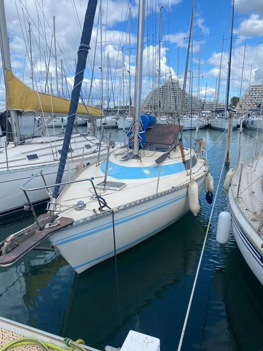 Challenger Bravo — Voilier blanc et bleu amarré dans une marina, vu de trois quarts avant.