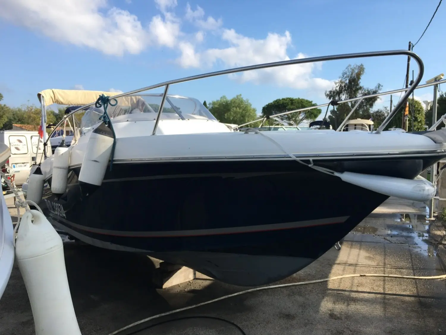 Jeanneau Cap Camarat 755 — Bateau à moteur blanc et bleu photographié à terre, entouré de pare-battages.