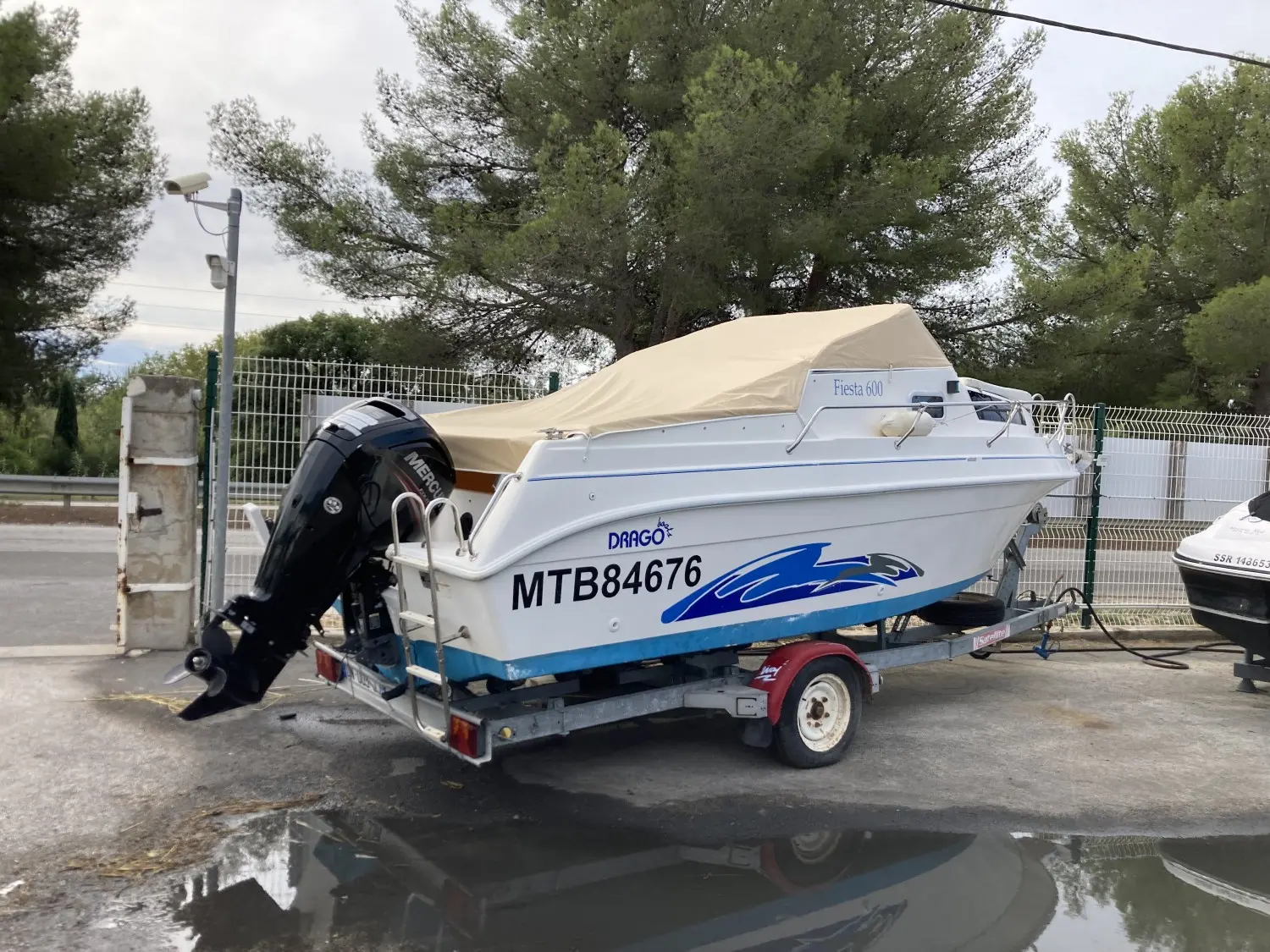 Drago Fiesta 600 — Bateau à cabine blanc et bleu, bâché, présenté sur remorque avec moteur hors-bord.