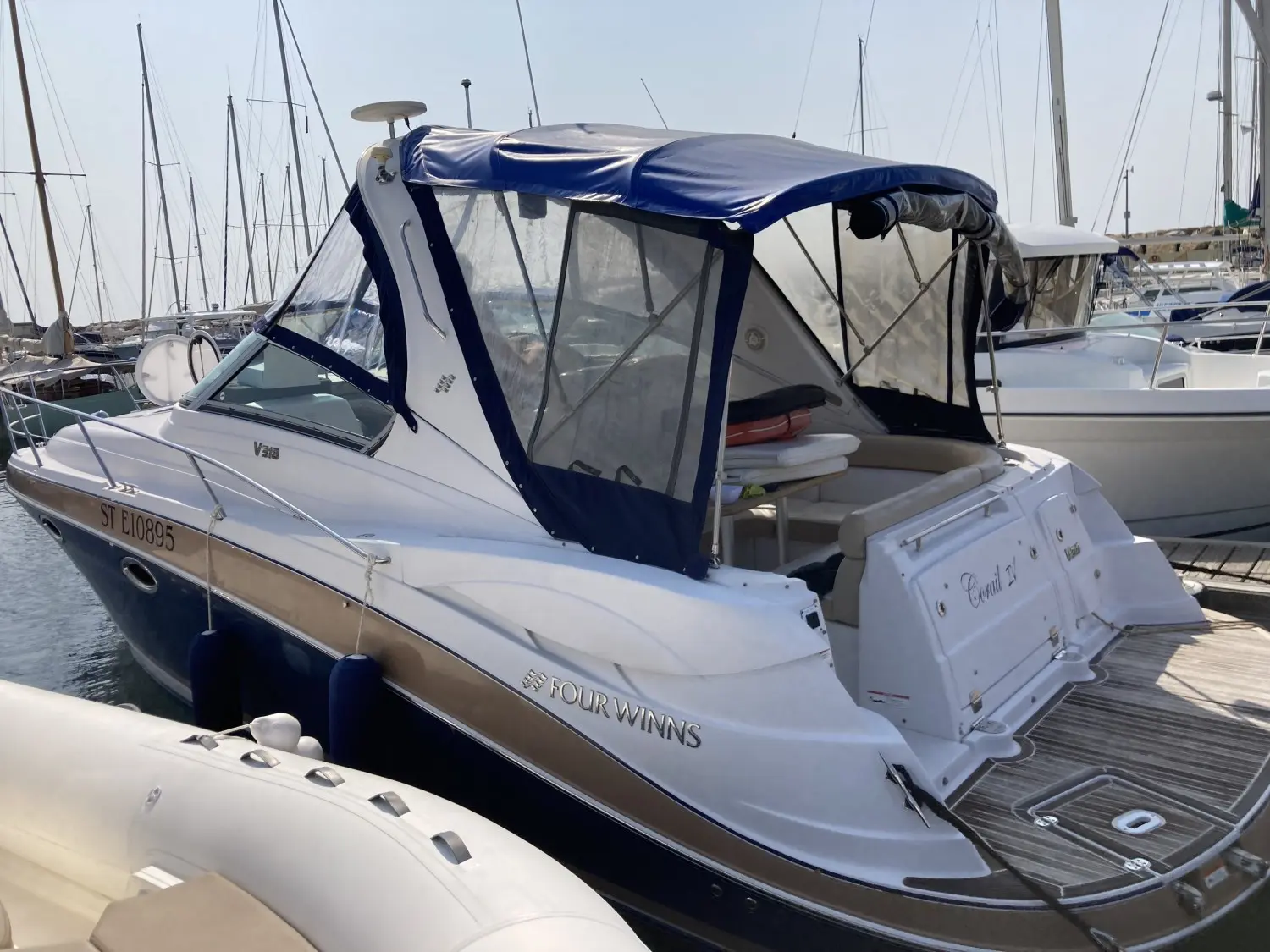 Four Winns Vista 318 — Bateau blanc à taud bleu amarré dans une marina, vu de trois quarts arrière.