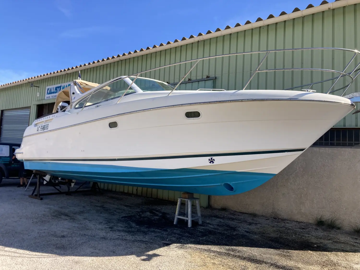 Jeanneau Prestige 34 — Bateau à moteur blanc et bleu photographié à terre devant un bâtiment industriel.