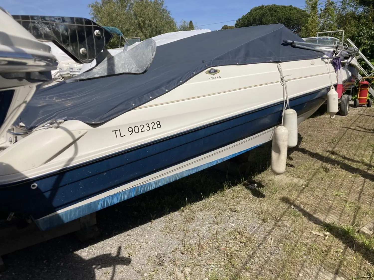 Bayliner Capri Cuddy 2052 — Vue latérale partielle d’un bateau à coque bleue, bâché et stationné à terre.