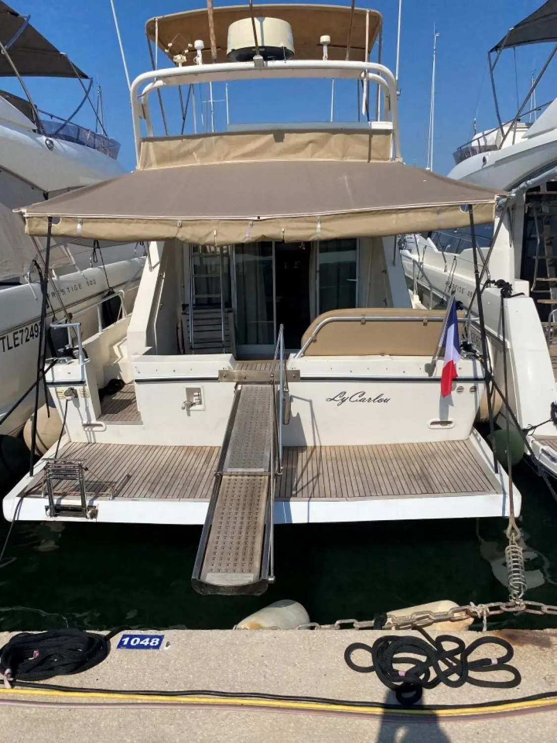 Guy Couach 1501 — Vue arrière d’un bateau à moteur amarré, avec passavant central et taud beige.