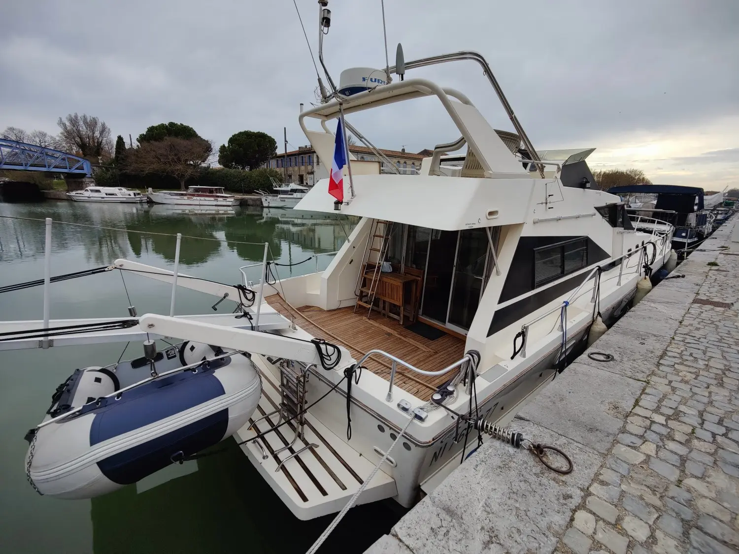 Guy Couach 1501 — Bateau à moteur blanc amarré le long d’un quai, vu depuis l’arrière bâbord.