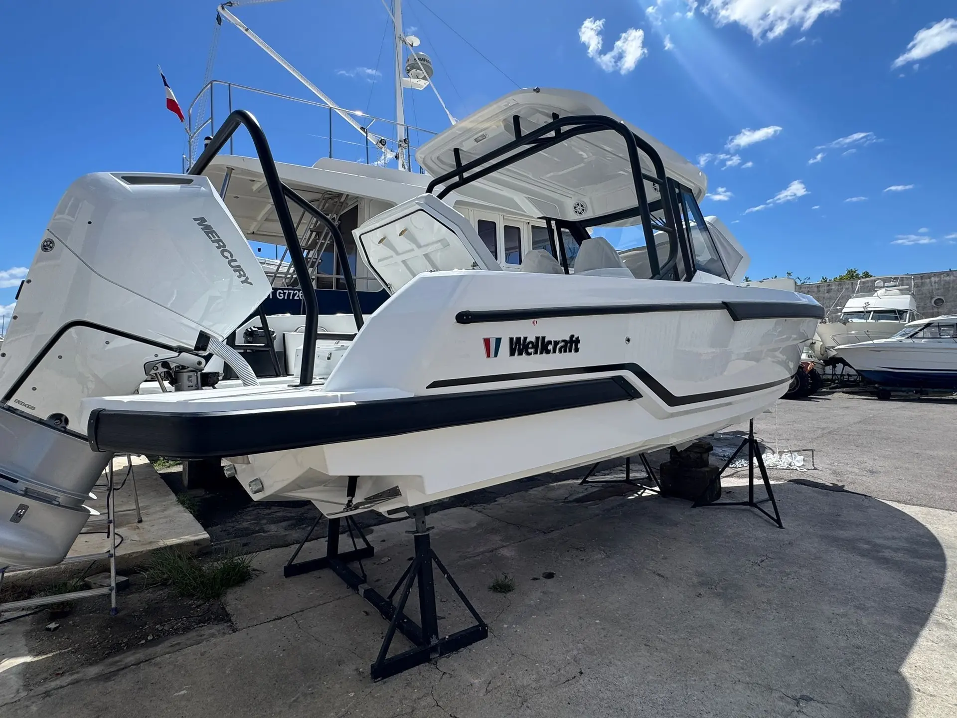 Wellcraft 28 T-Top — Bateau blanc à cabine et moteur hors-bord présenté à terre dans un chantier nautique.