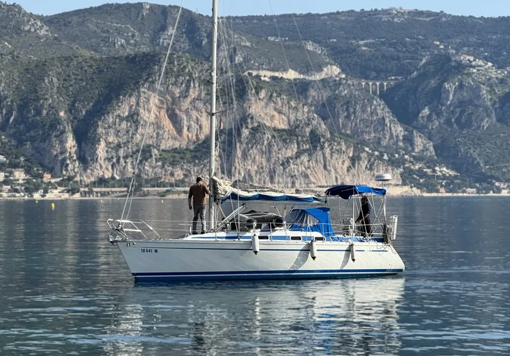 Bavaria 320 Sportline — Voilier blanc et bleu sur une eau calme, avec deux personnes à bord.