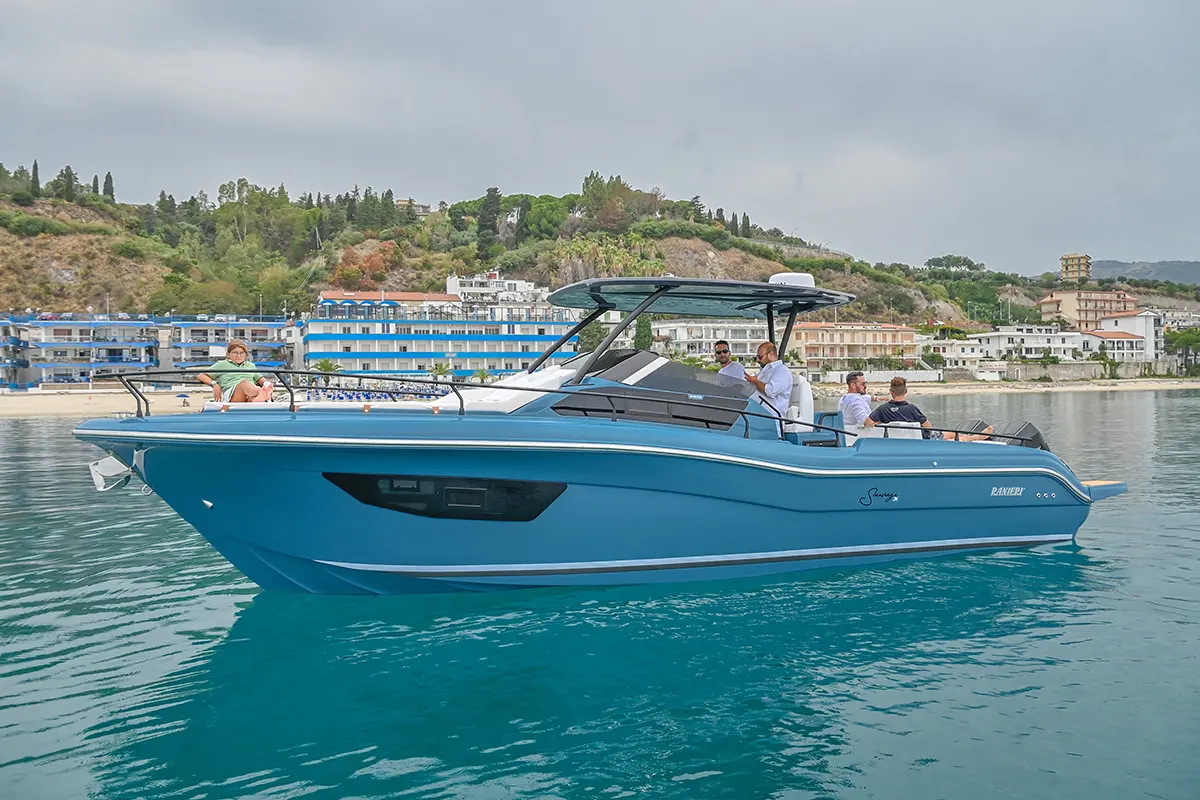 Ranieri Sauvage 34 Spider — Bateau à moteur bleu vu de profil dans un port, avec plusieurs personnes à bord.