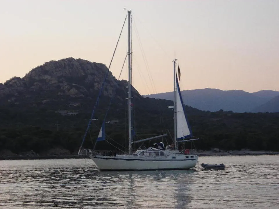 Siltala Yachts Nauticat 43 — Voilier blanc au mouillage devant une côte rocheuse, avec une annexe à tribord.