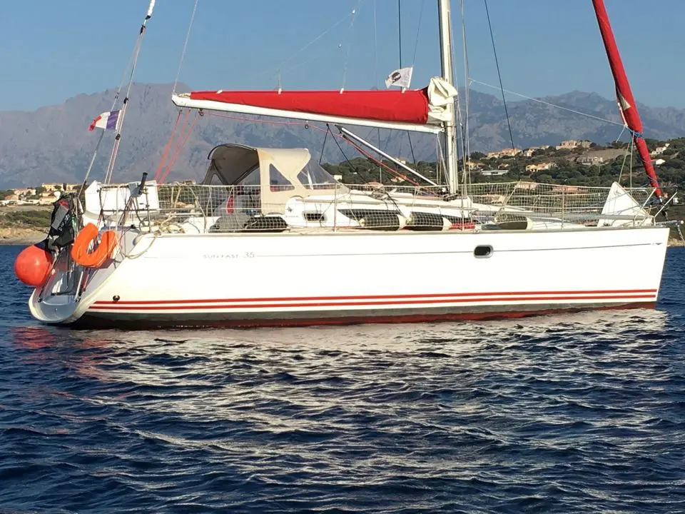 Jeanneau Sun Fast 35 — Voilier blanc à bandes rouges naviguant devant une côte montagneuse.