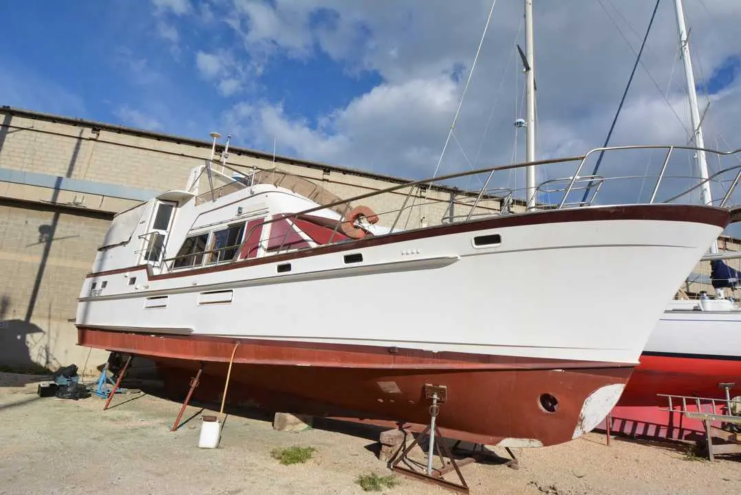 Island Gypsy 49 — Bateau à moteur blanc et rouge photographié à sec devant un bâtiment industriel.