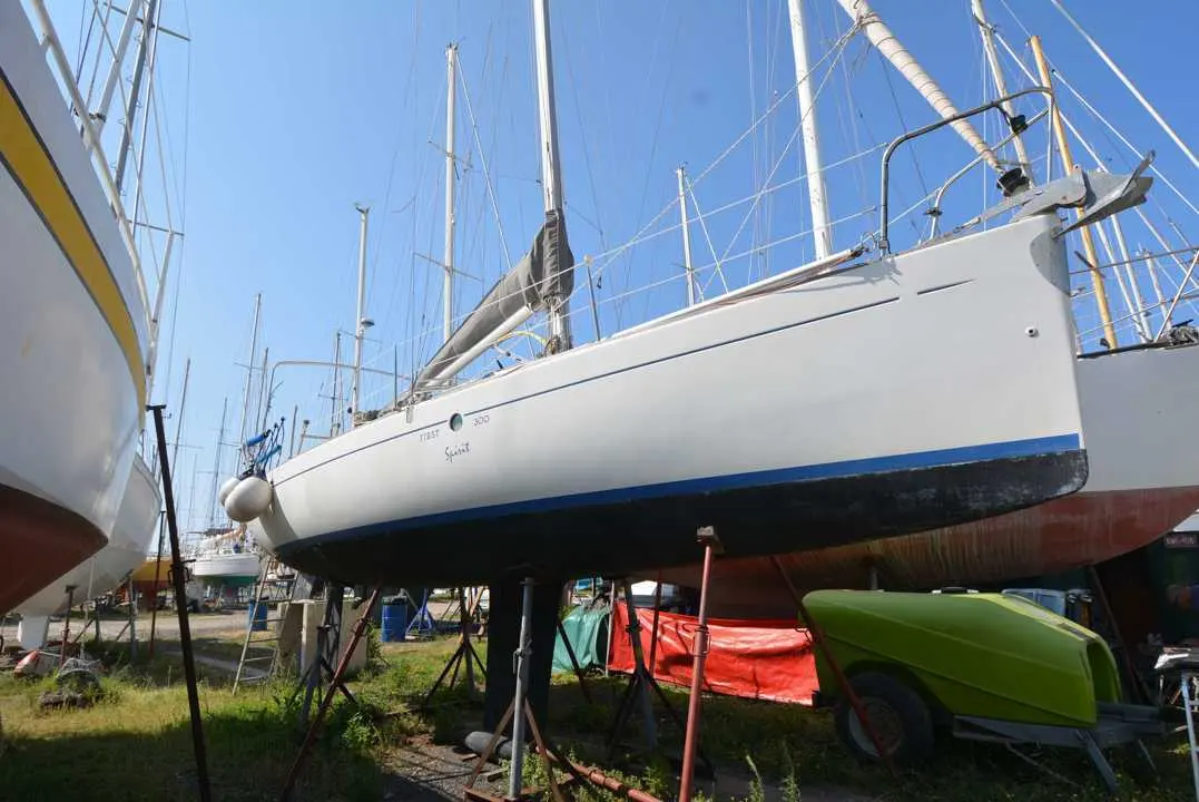 Beneteau First 300 Spirit — Voilier blanc à coque bleue, photographié à terre dans un chantier nautique.