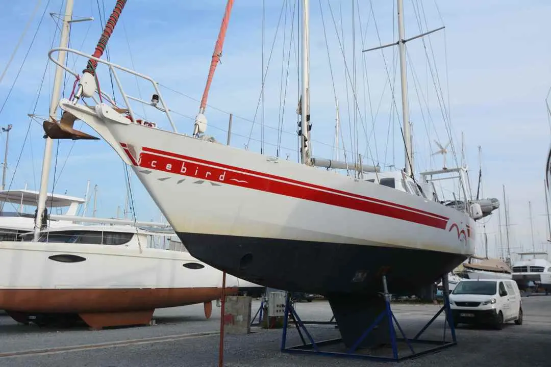 Meta Dalu 47 — Voilier blanc à bandes rouges présenté à terre dans un port à sec.