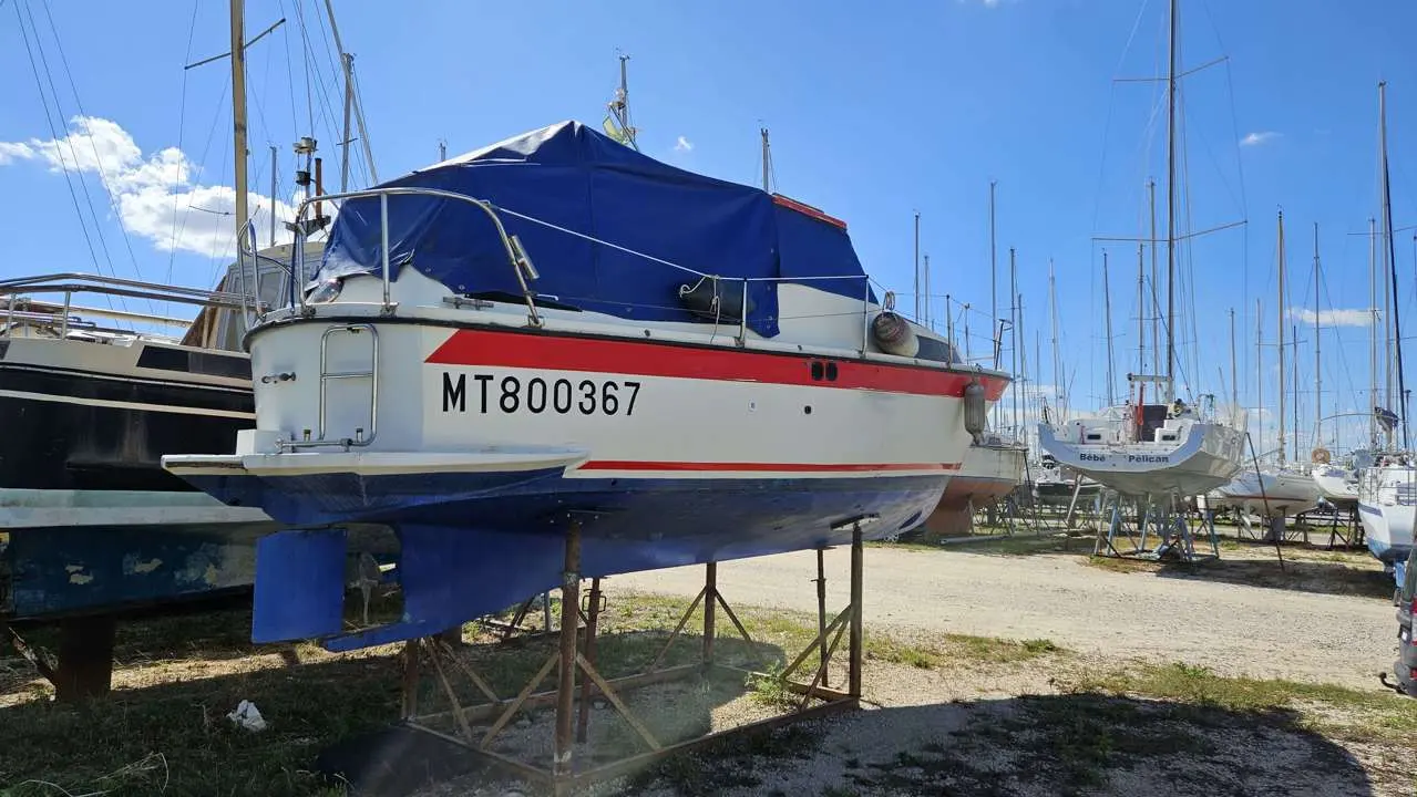 Bonum 25 — Bateau blanc et rouge bâché, photographié à terre dans un chantier naval.