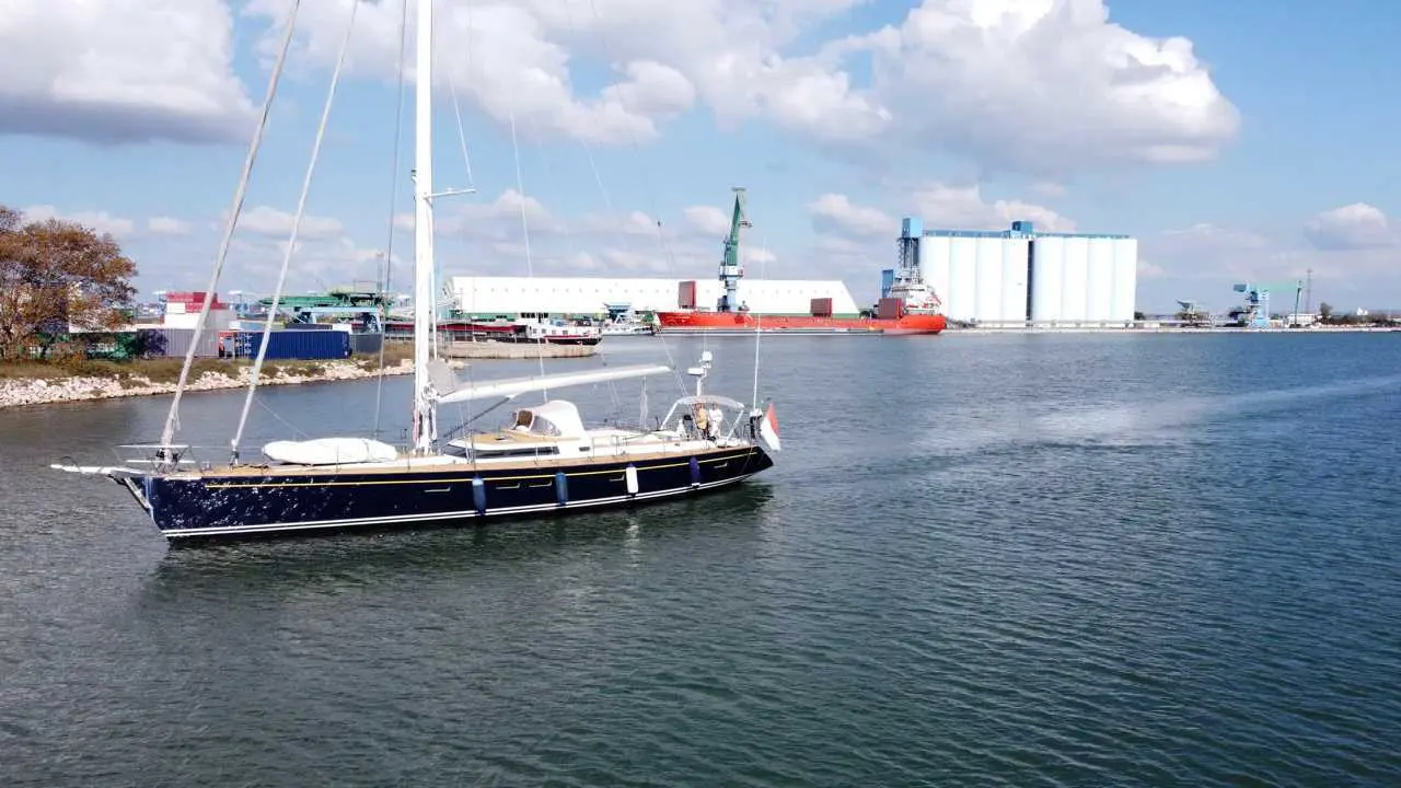 Cnb 70 — Voilier bleu amarré devant une zone portuaire industrielle.