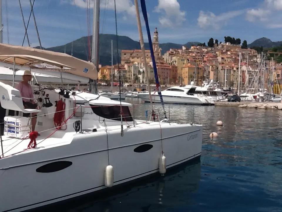Fountaine Pajot Mahe 36 — Catamaran blanc amarré dans un port, avec un village côtier en arrière-plan.