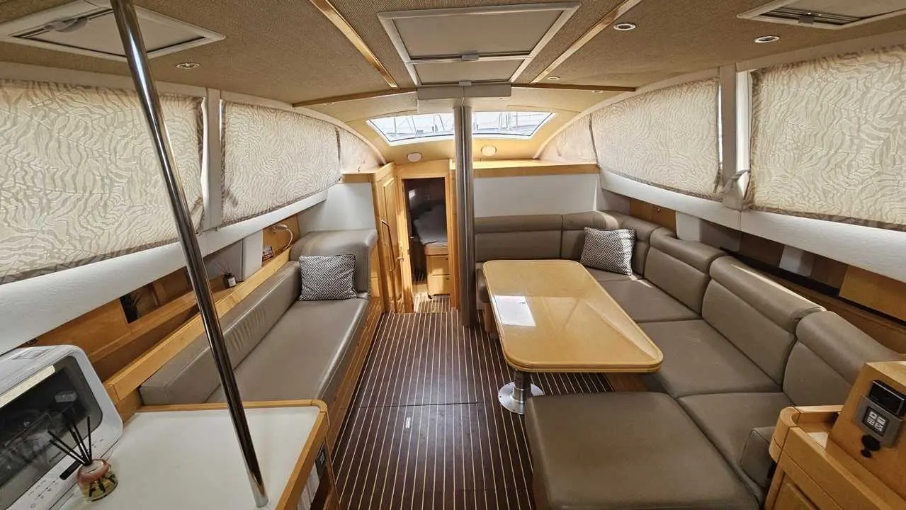 Alliaura Marine Feeling 48 — Salon intérieur d’un bateau avec banquettes, table, hublots et rangements en bois.