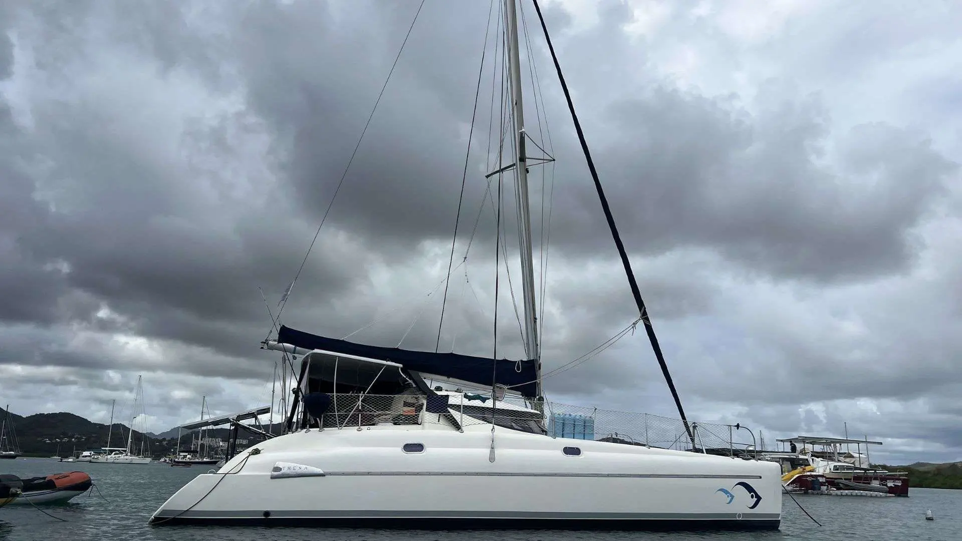 Fountaine Pajot Athena 38 — Catamaran blanc vu de profil, amarré dans une marina sous un ciel nuageux.
