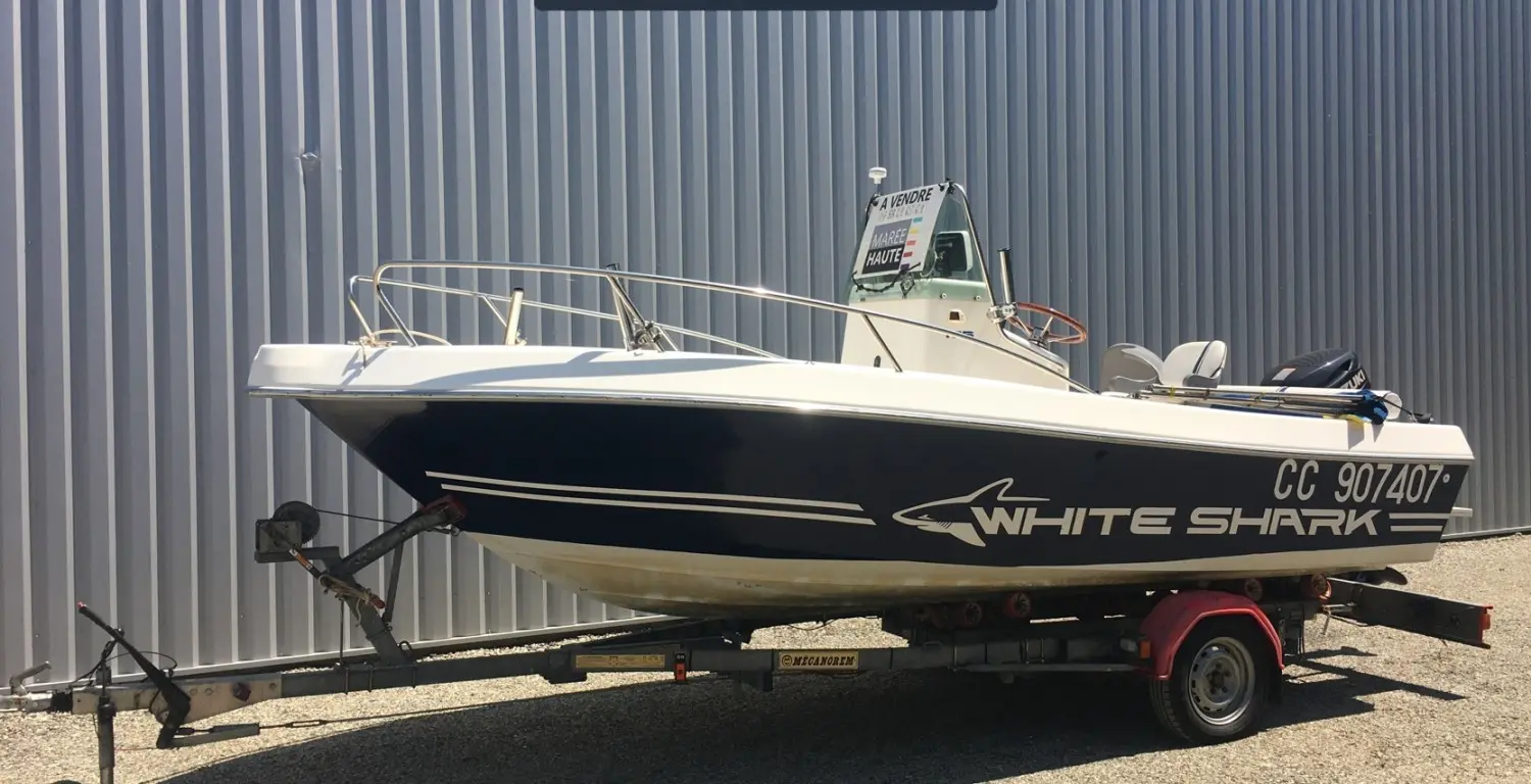 White Shark 175 — Bateau à moteur blanc et bleu présenté sur une remorque devant un bâtiment.