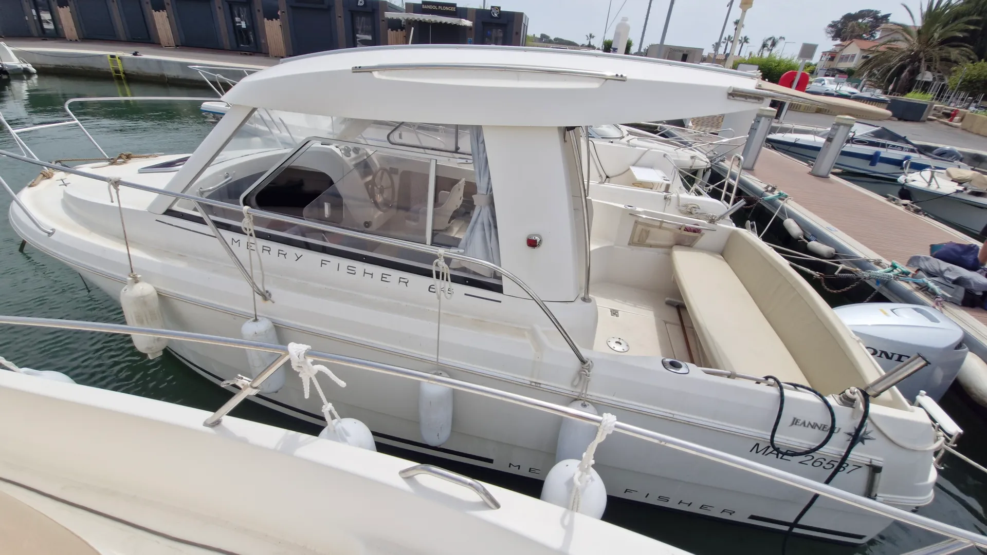 Jeanneau Merry Fisher 645 — Bateau à moteur blanc amarré au ponton, vu de trois quarts.