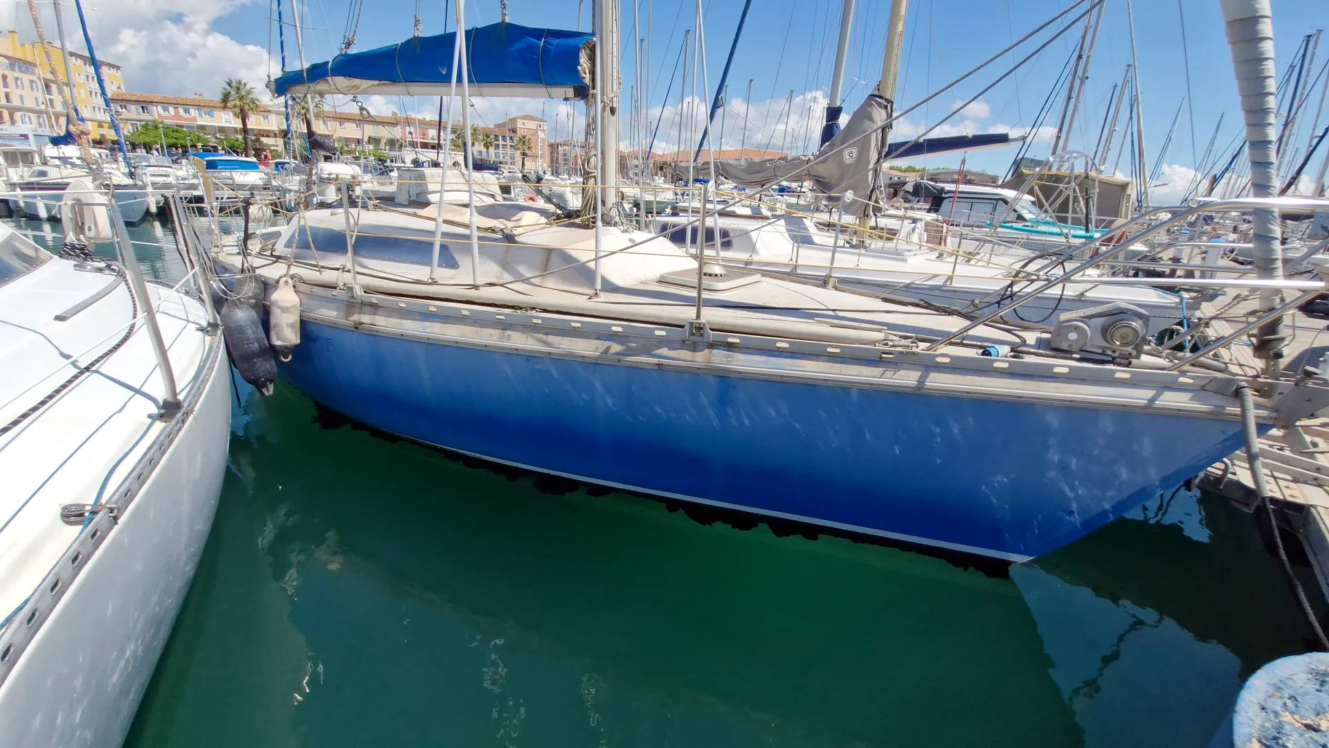 Jeanneau Aquila — Voilier bleu amarré dans un port, vu de côté entre d’autres bateaux.