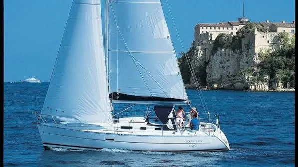 Beneteau OCEANIS 323 — Voilier blanc sous voiles, photographié au large d'une côte rocheuse.