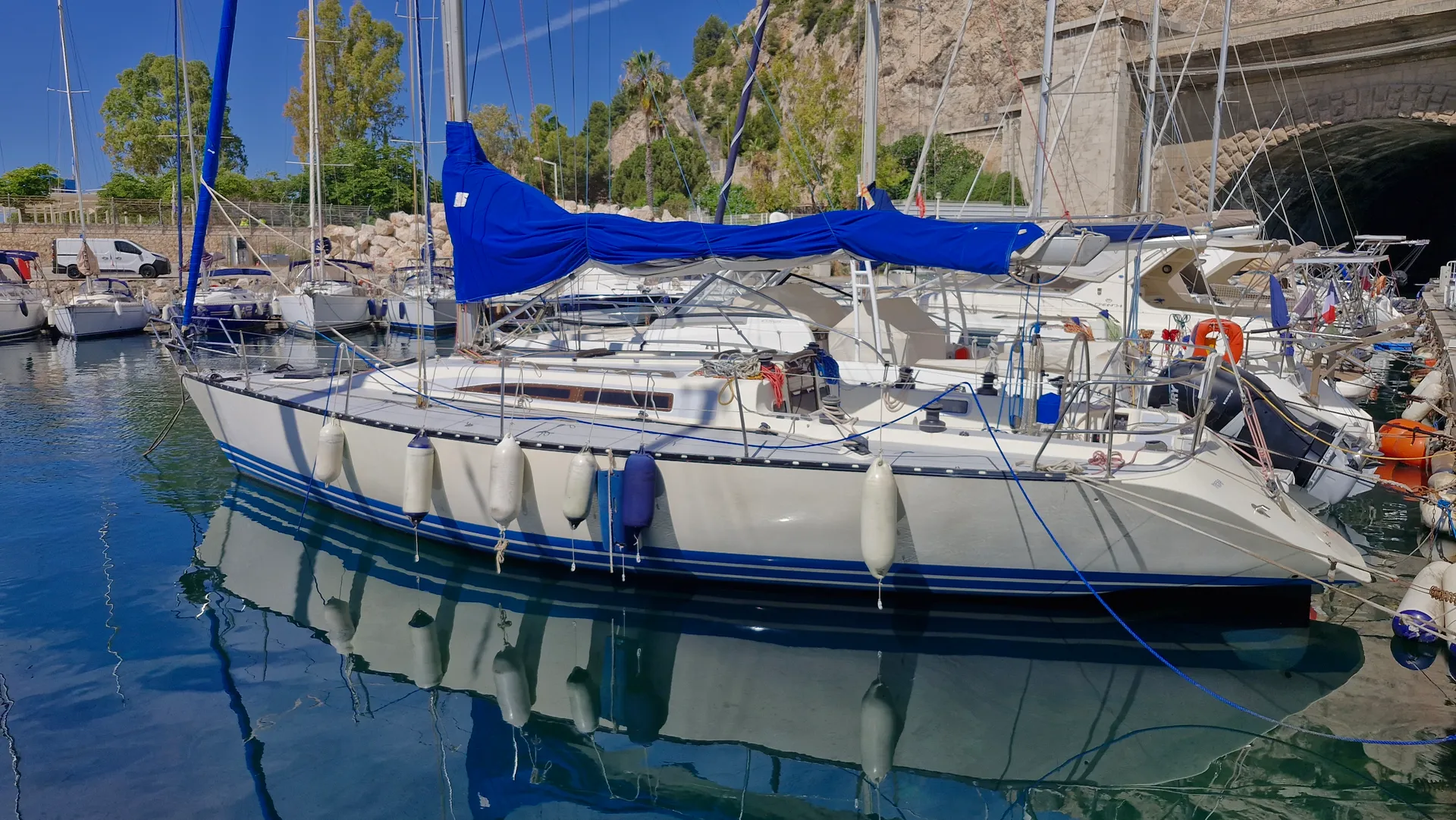 X-Yachts X-402 — Voilier amarré vu de profil dans une marina, avec capote bleue et défenses.
