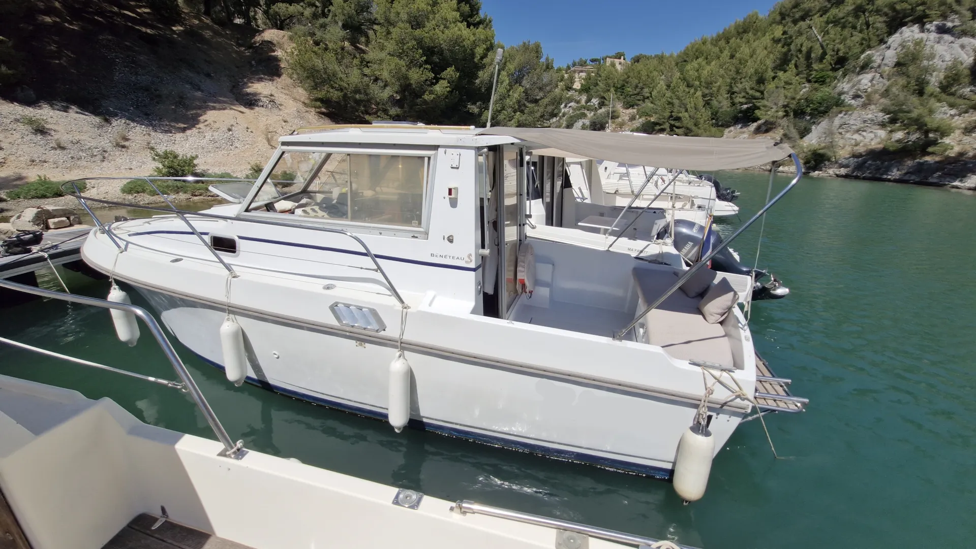 Beneteau Antares 730 — Bateau blanc à cabine amarré dans une crique boisée, vu de trois quarts.