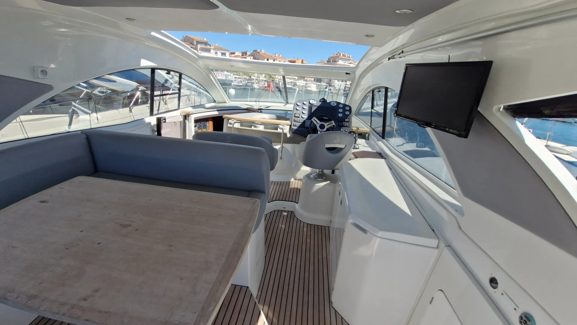 Beneteau GT 44 — Vue intérieure du poste de pilotage et du salon d’un bateau, avec écran et banquette.