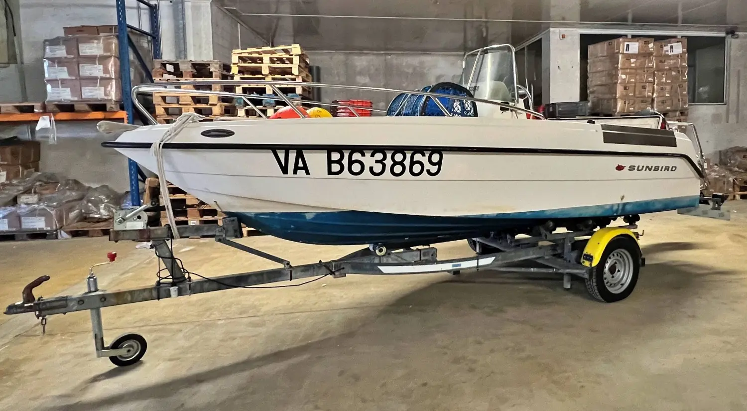 Kelt Sunbird 160 — Bateau à moteur blanc et bleu présenté sur une remorque dans un entrepôt.