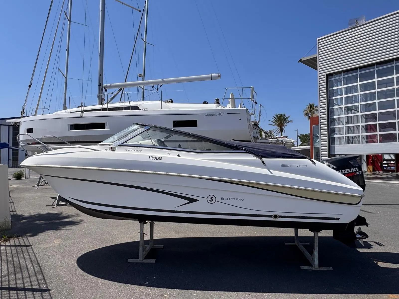 Beneteau Flyer 650 Cabrio — Bateau à moteur blanc présenté sur berceau devant un voilier.