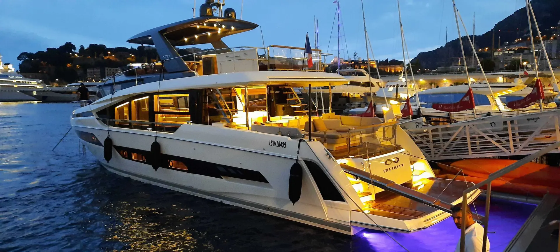 Prestige Yachts X70 — Vue trois quarts arrière d’un yacht à moteur amarré dans un port au crépuscule.