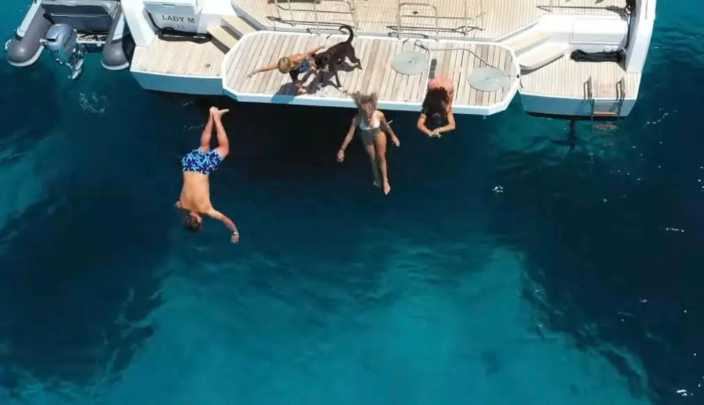Lagoon 55 — Vue aérienne d’une plateforme arrière avec trois personnes dans l’eau.