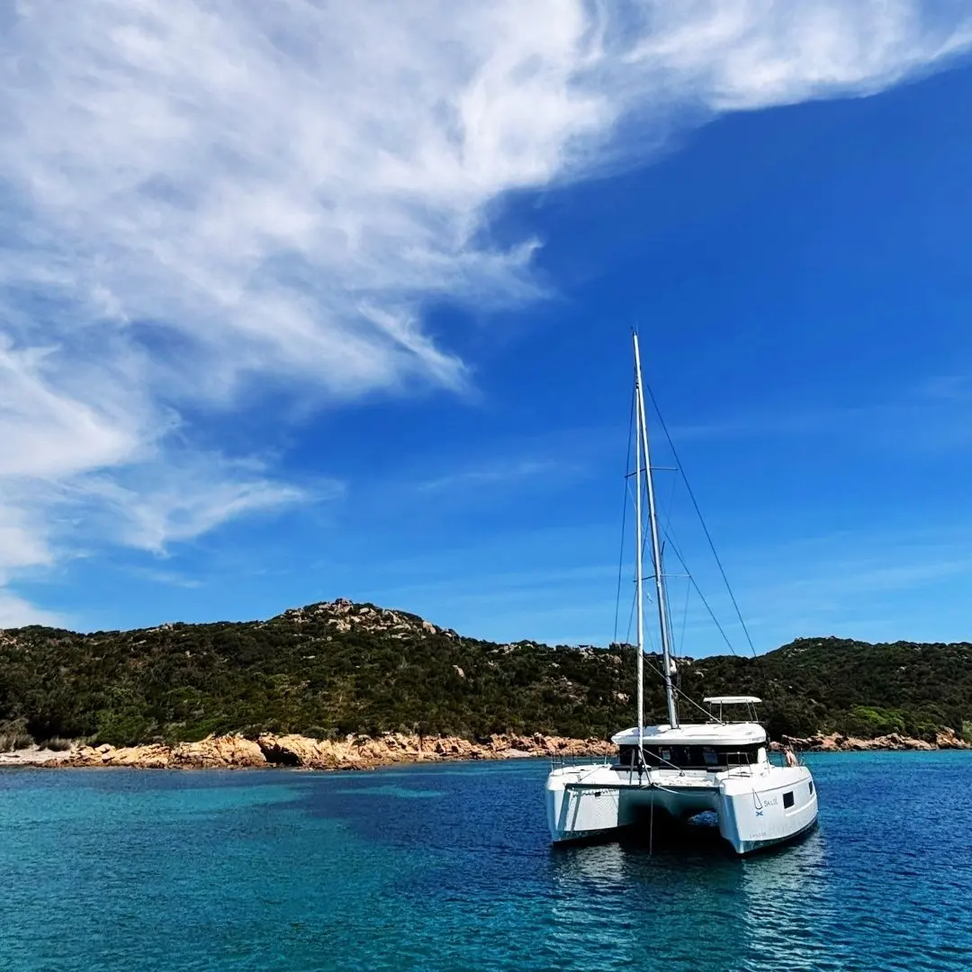 Lagoon 38 — Un catamaran blanc est mouillé devant une côte rocheuse, sous un ciel dégagé.