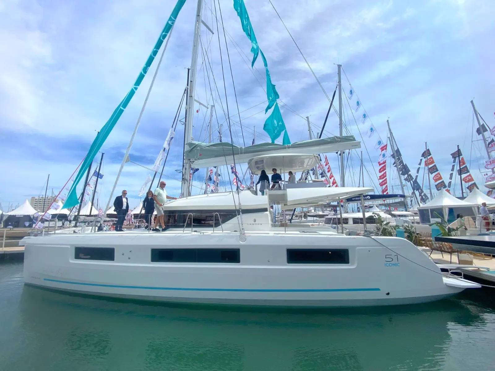 Lagoon 51 — Catamaran blanc amarré dans un salon nautique, avec plusieurs personnes à bord.