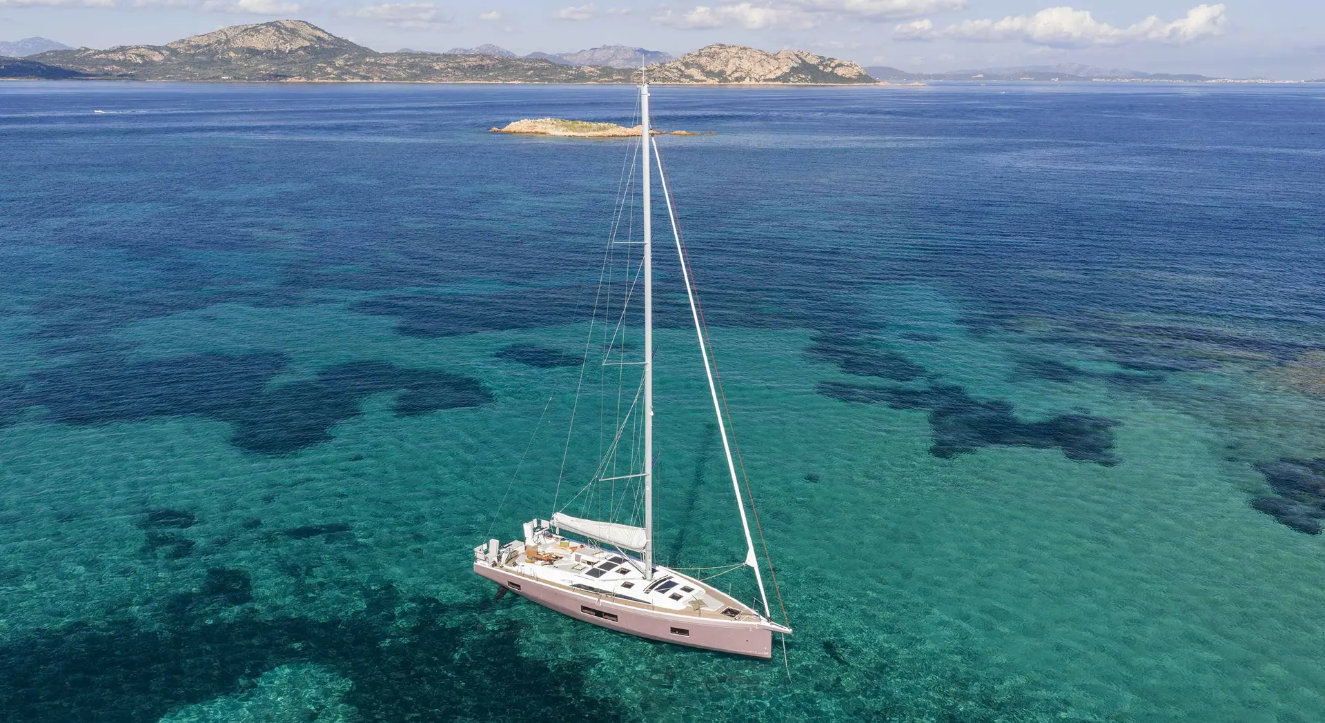 Beneteau Oceanis 52 — Voilier photographié en mer turquoise, avec une côte montagneuse en arrière-plan.